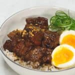Filipino pork adobo topped on rice and sliced soft boiled egg in a bowl.
