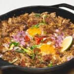 Pork Belly Sisig with Egg and lime on a skillet.