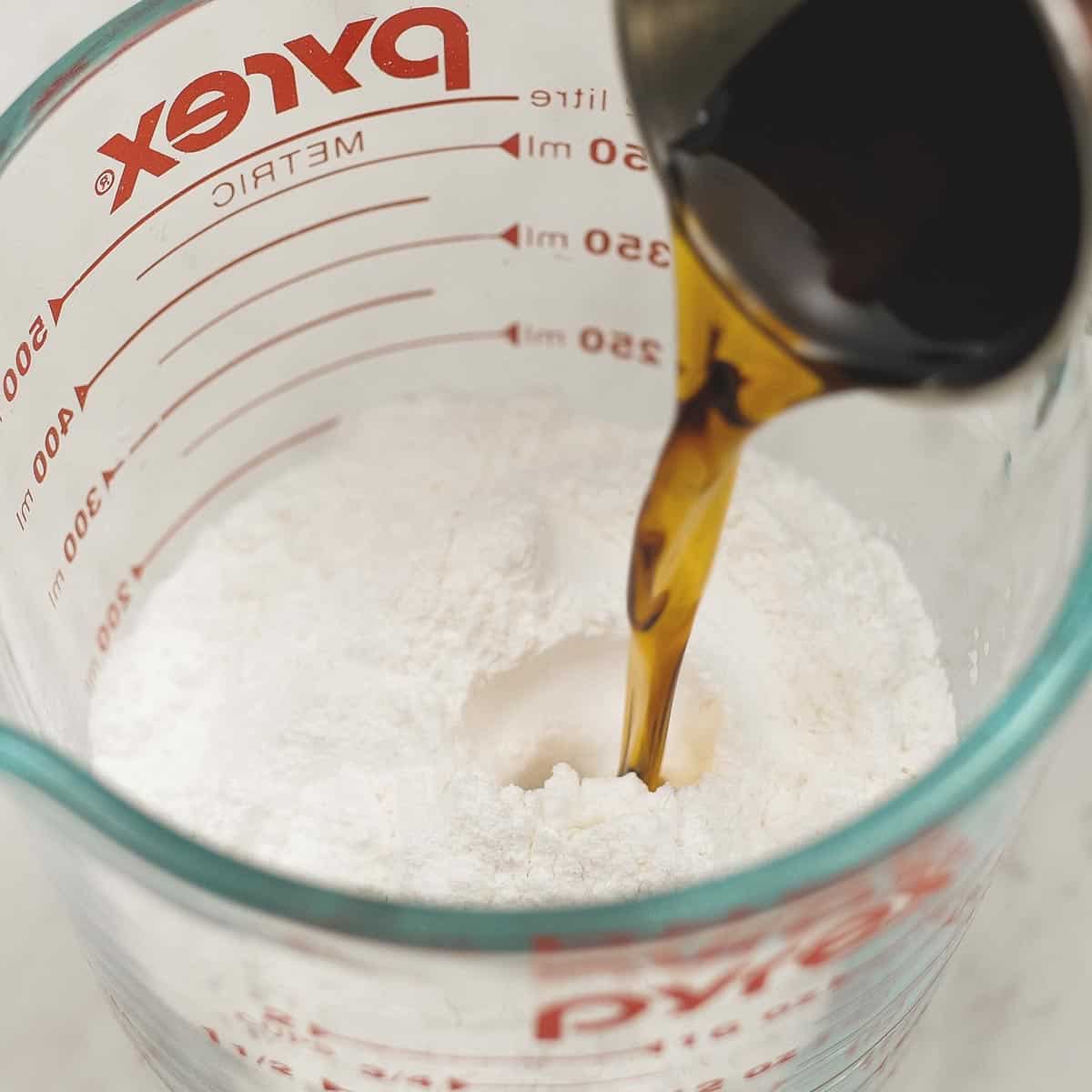 Adding fish sauce to the flour and other ingredients in the cup.
