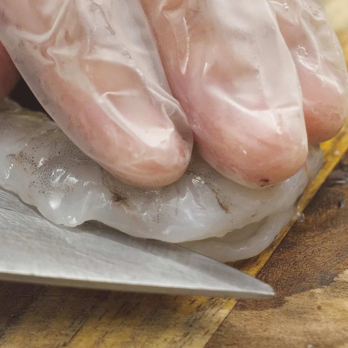 Splitting a peeled, deveined shrimp in half using a knife.