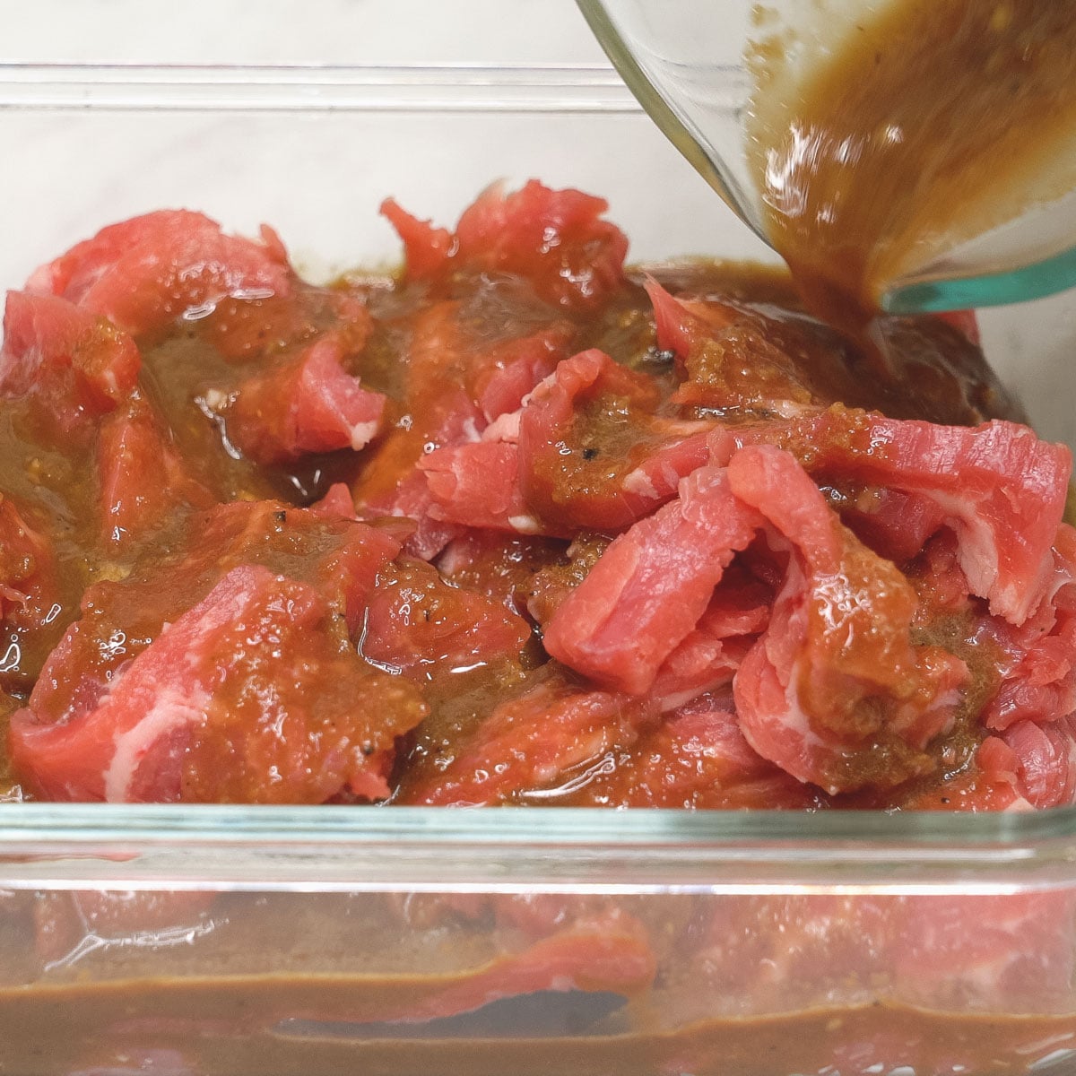 Pouring the marinade over the meat in the glass container.