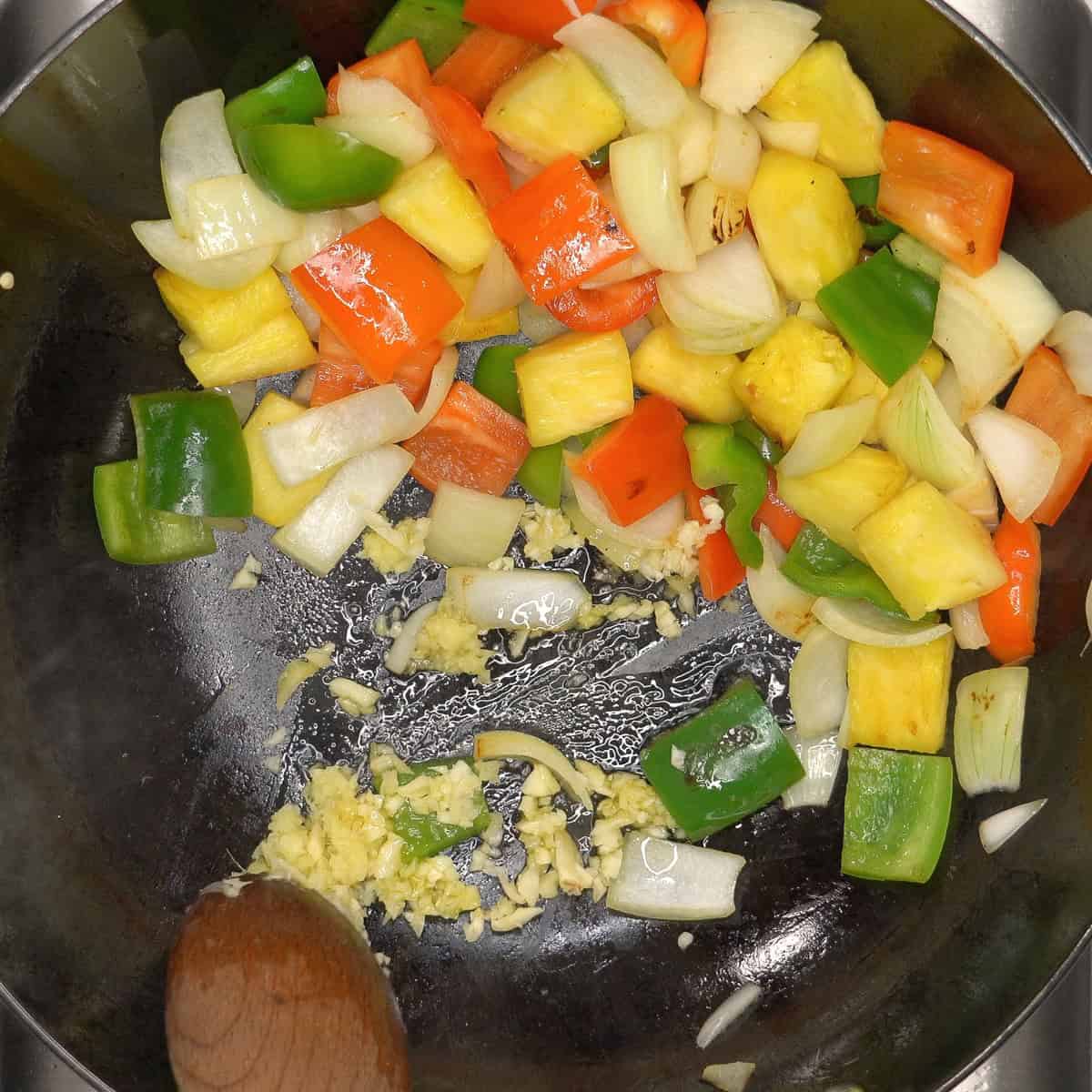 Sauteing ginger and garlic in the wok with pineapple and vegetables pushed aside.