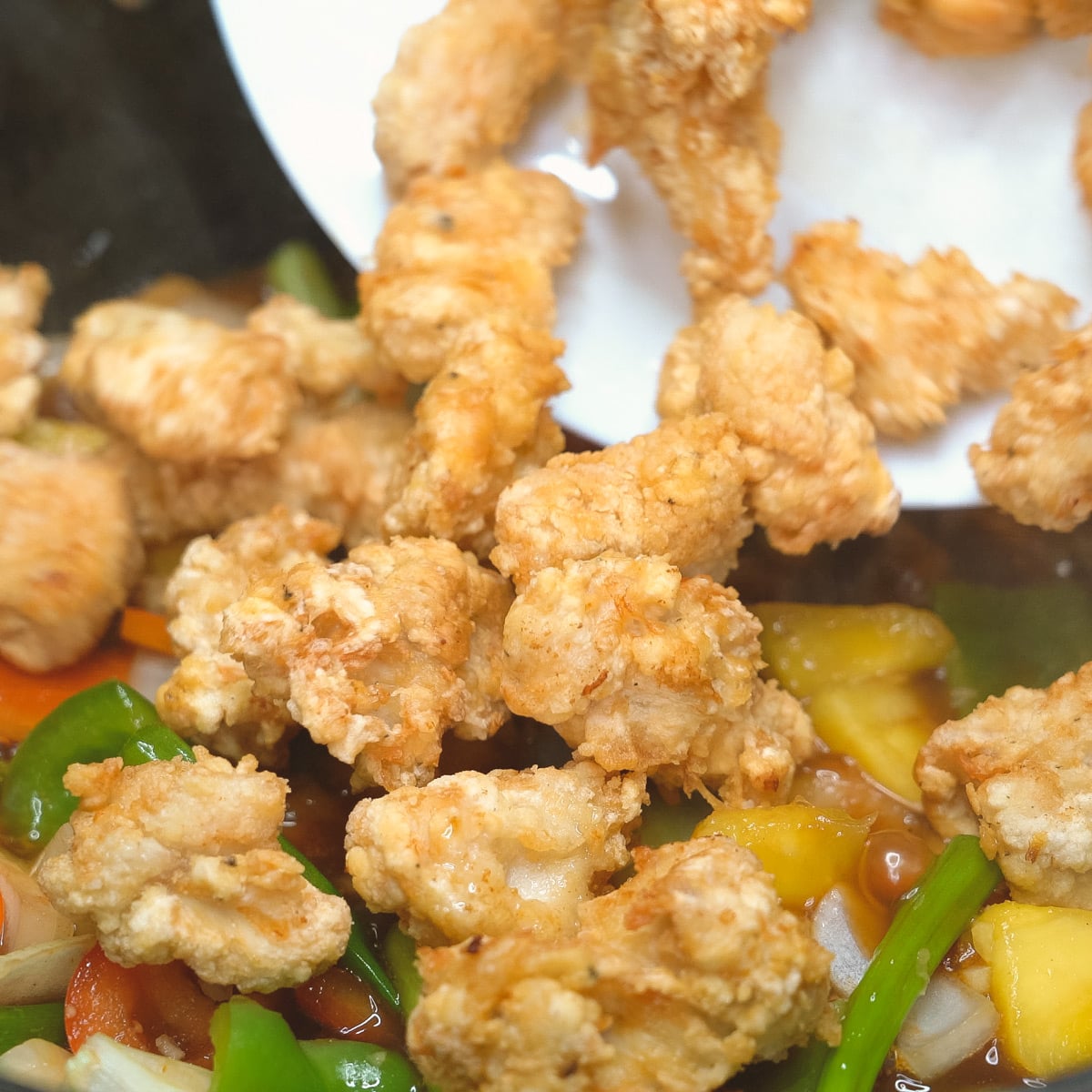 Adding the fried chicken to the pineapples and vegetables.