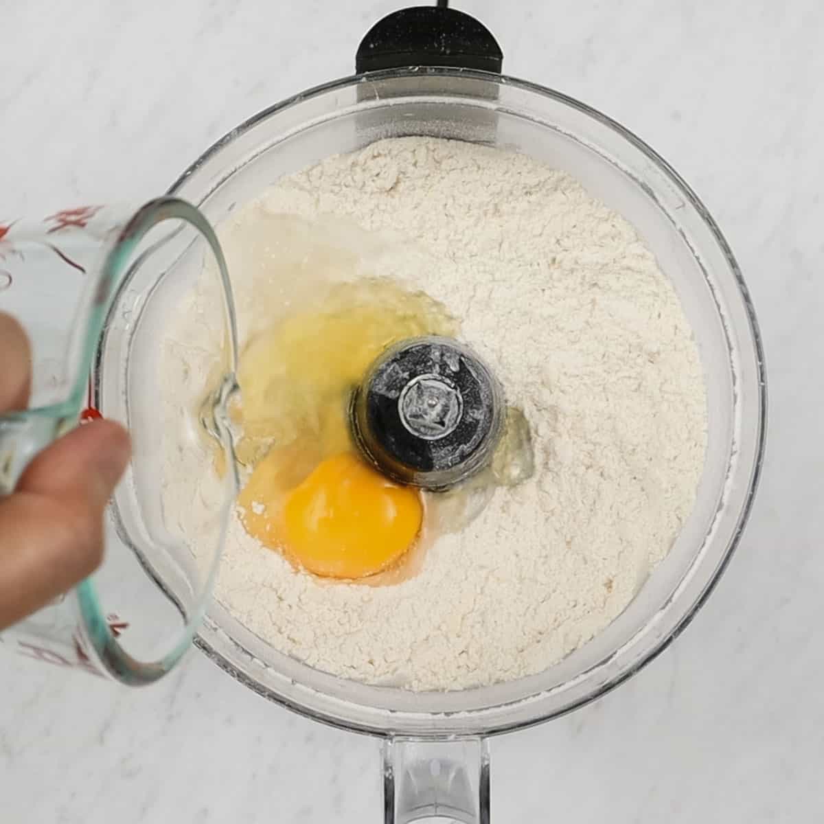 Adding egg to the flour mixture in the food processor.