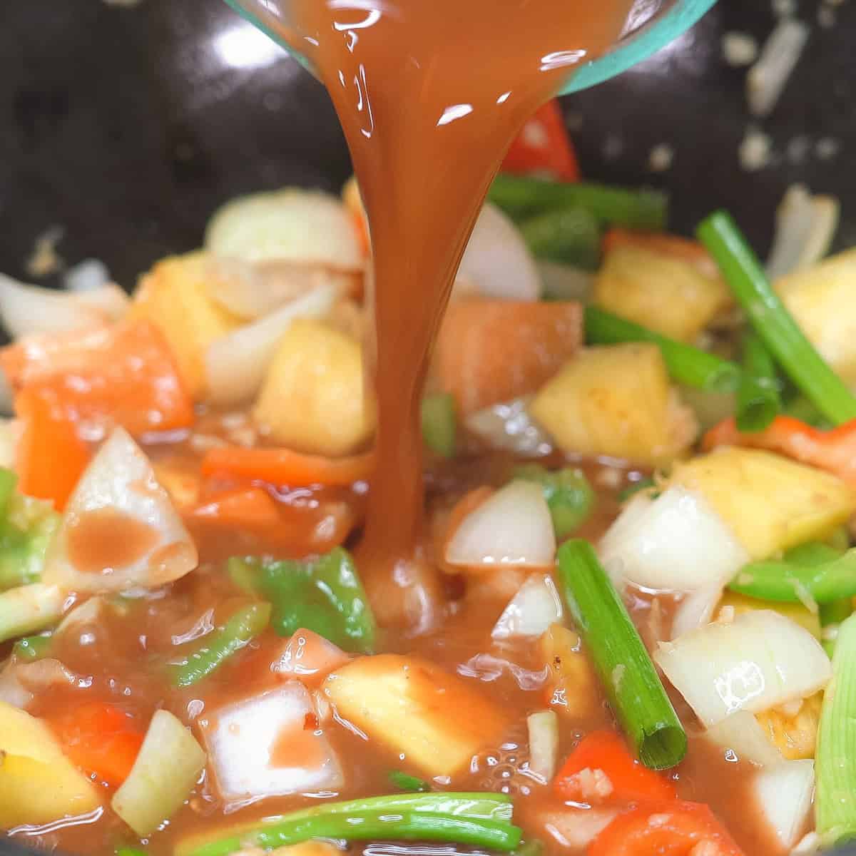 Pouring the sauce over the pineapple and vegetables in the wok. 