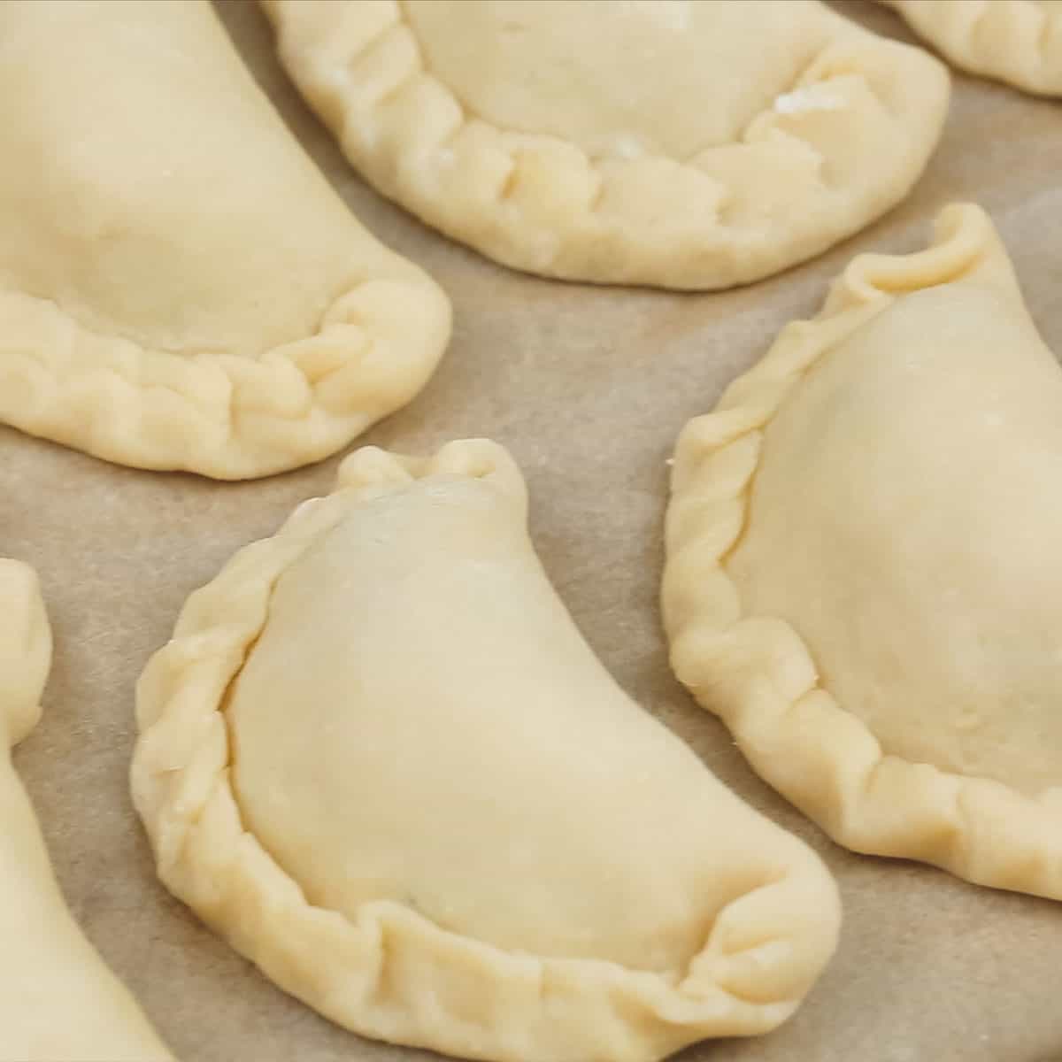 Uncooked chicken empanadas on a parchment paper-lined baking sheet.
