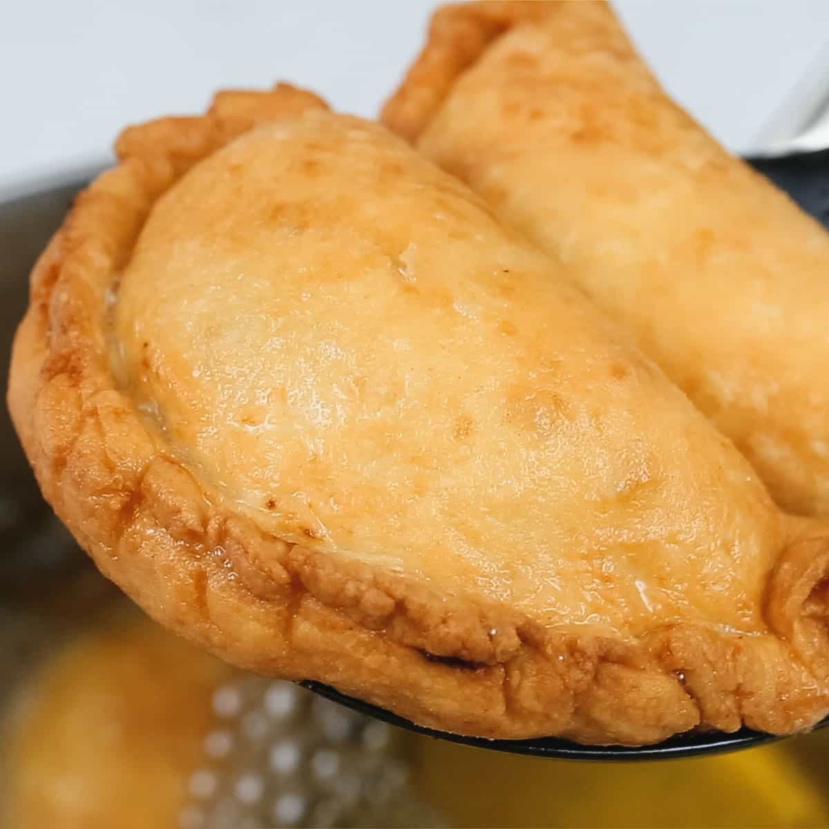 Draining fried empanadas on a slotted spoon.