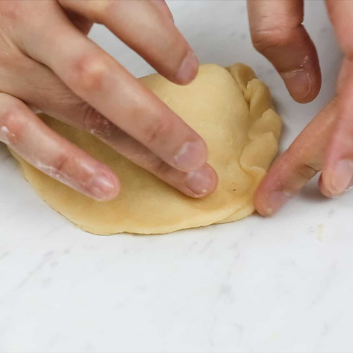 Creating pleats on the edges of a chicken empanada.