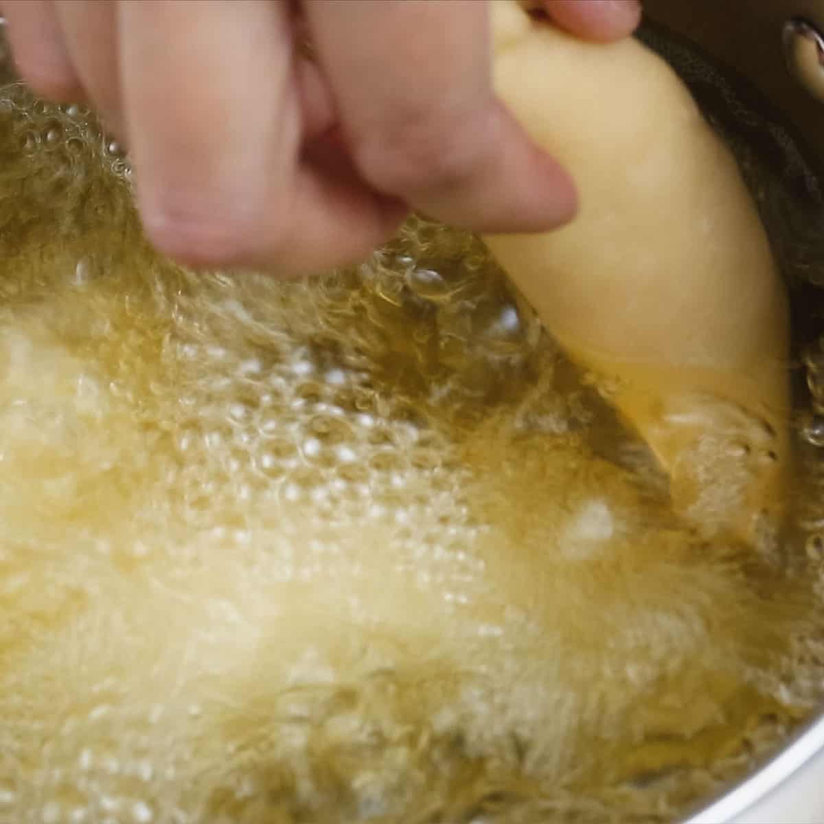 Dropping empanada in a pot of hot oil.