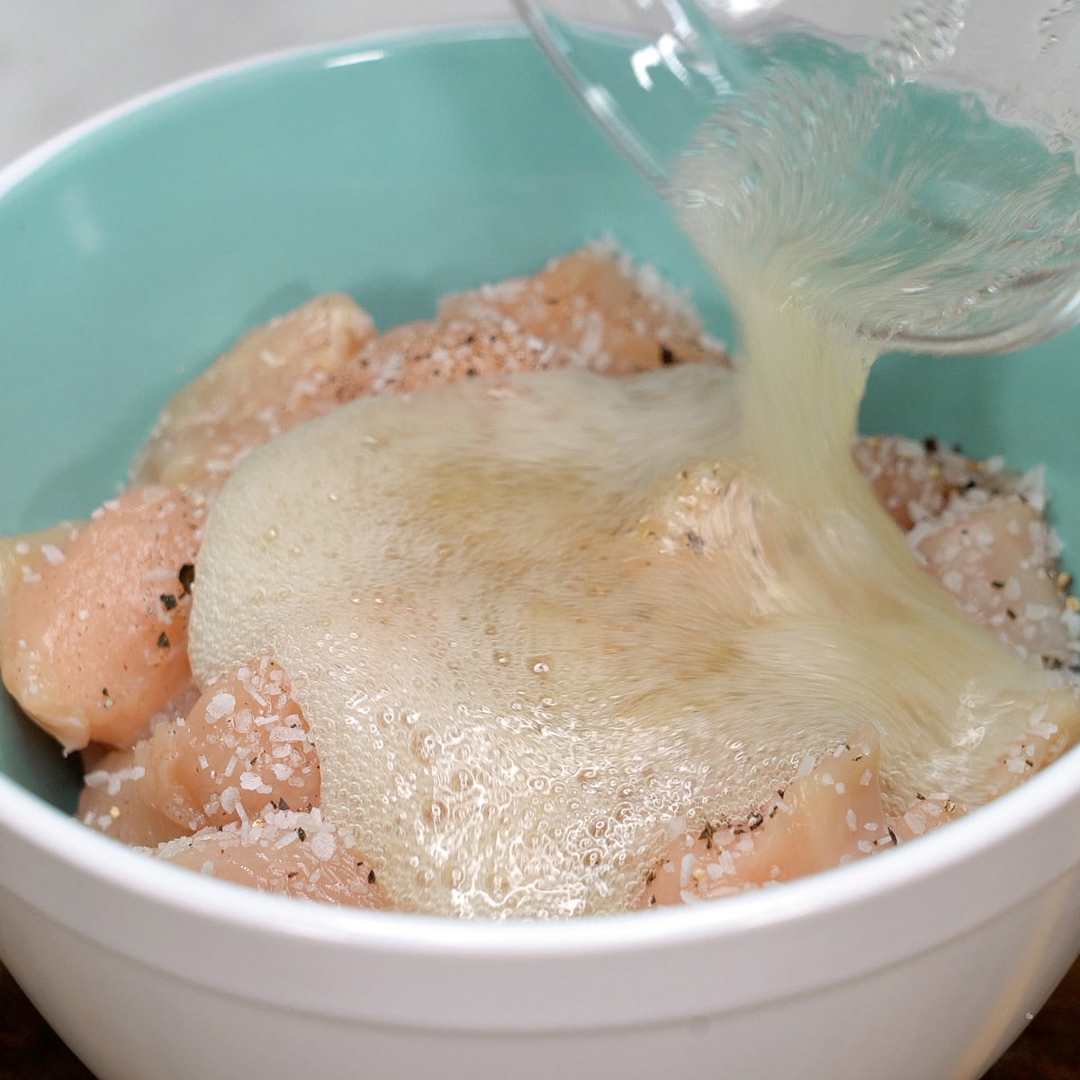 Adding the beaten egg white to the cut up chicken in the bowl. 