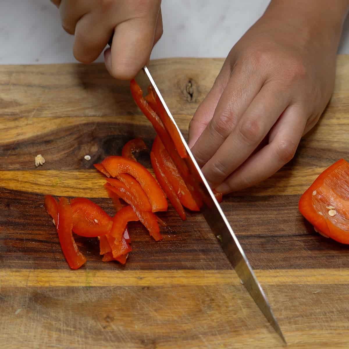Slicing red bell pepper thinly.