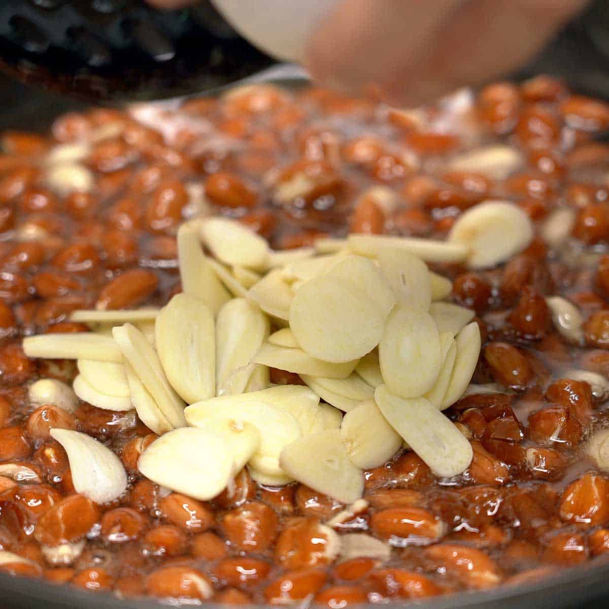 Adding garlic slices to the peanuts in oil.