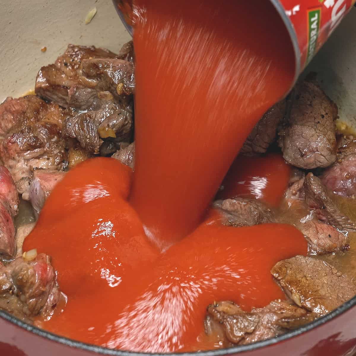 Adding tomatoes to the meat in the pot.