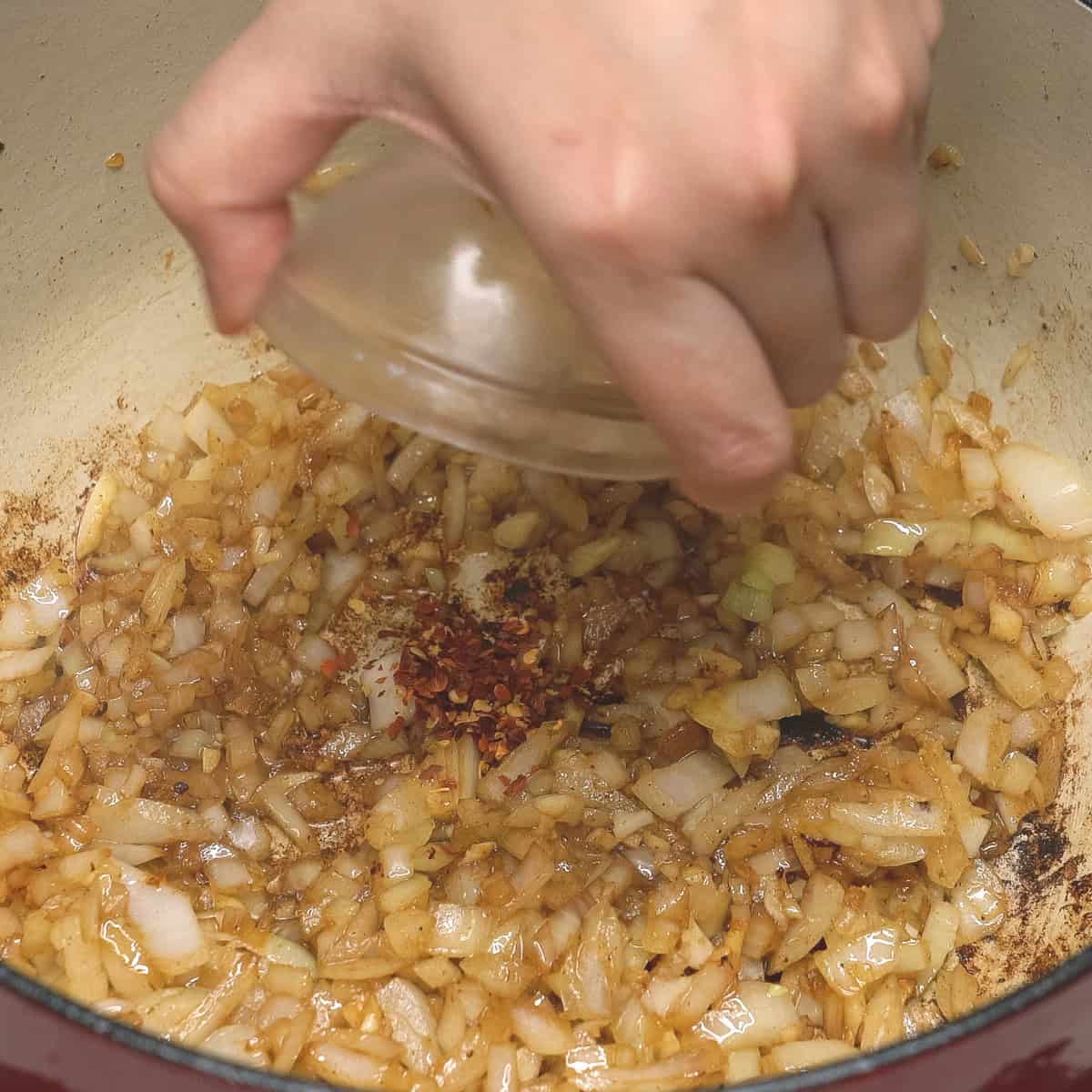 Adding crushed red pepper to the sauteed garlic and onions.