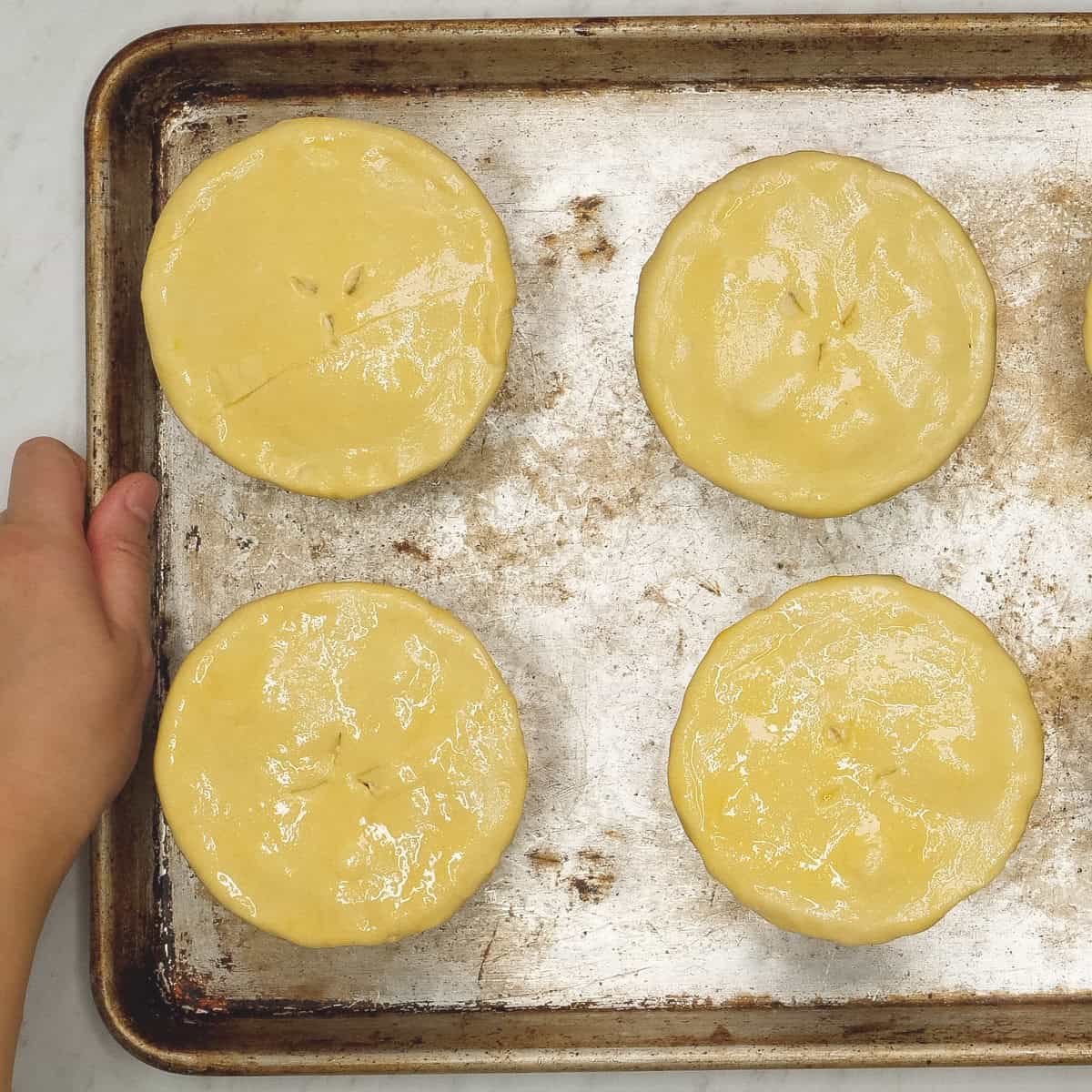 Unbaked individual portions of chicken pot pie with puff pastry on a baking sheet.