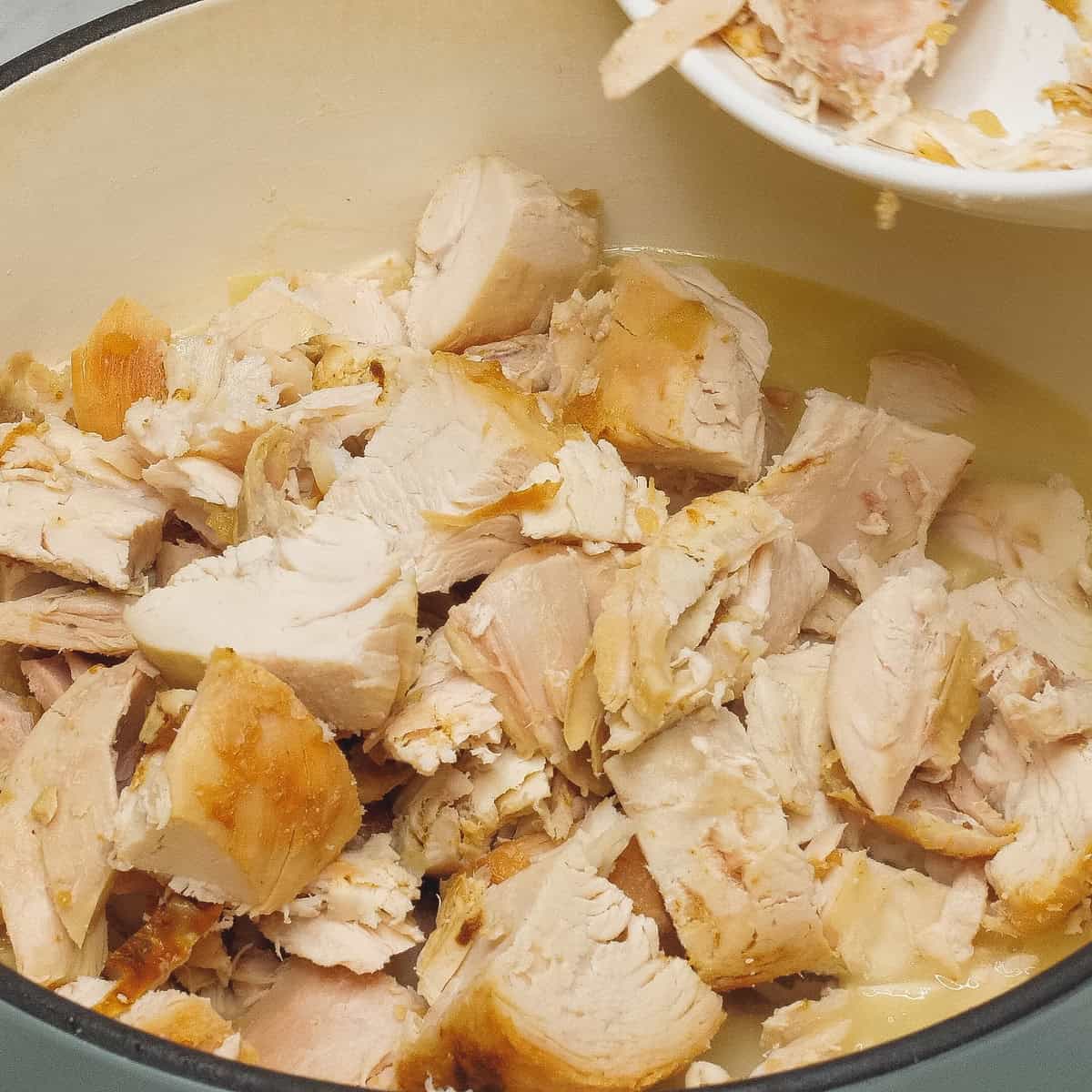 Adding the chunks of chicken to the mixture in the pot.