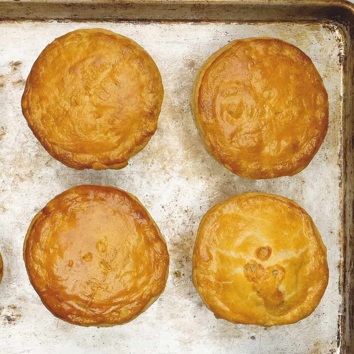 Baked individual portions of chicken pot pie with puff pastry on a baking sheet.