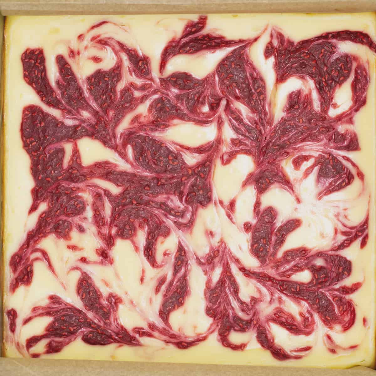 Baked cheesecake with raspberry swirl on a pan.