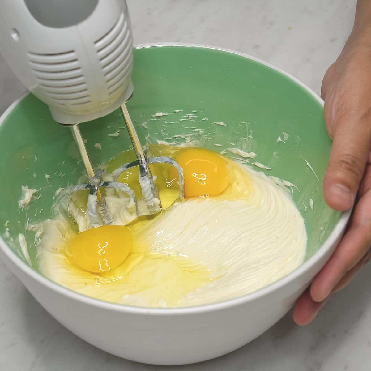 Beating eggs into the batter with an hand mixer in the bowl.