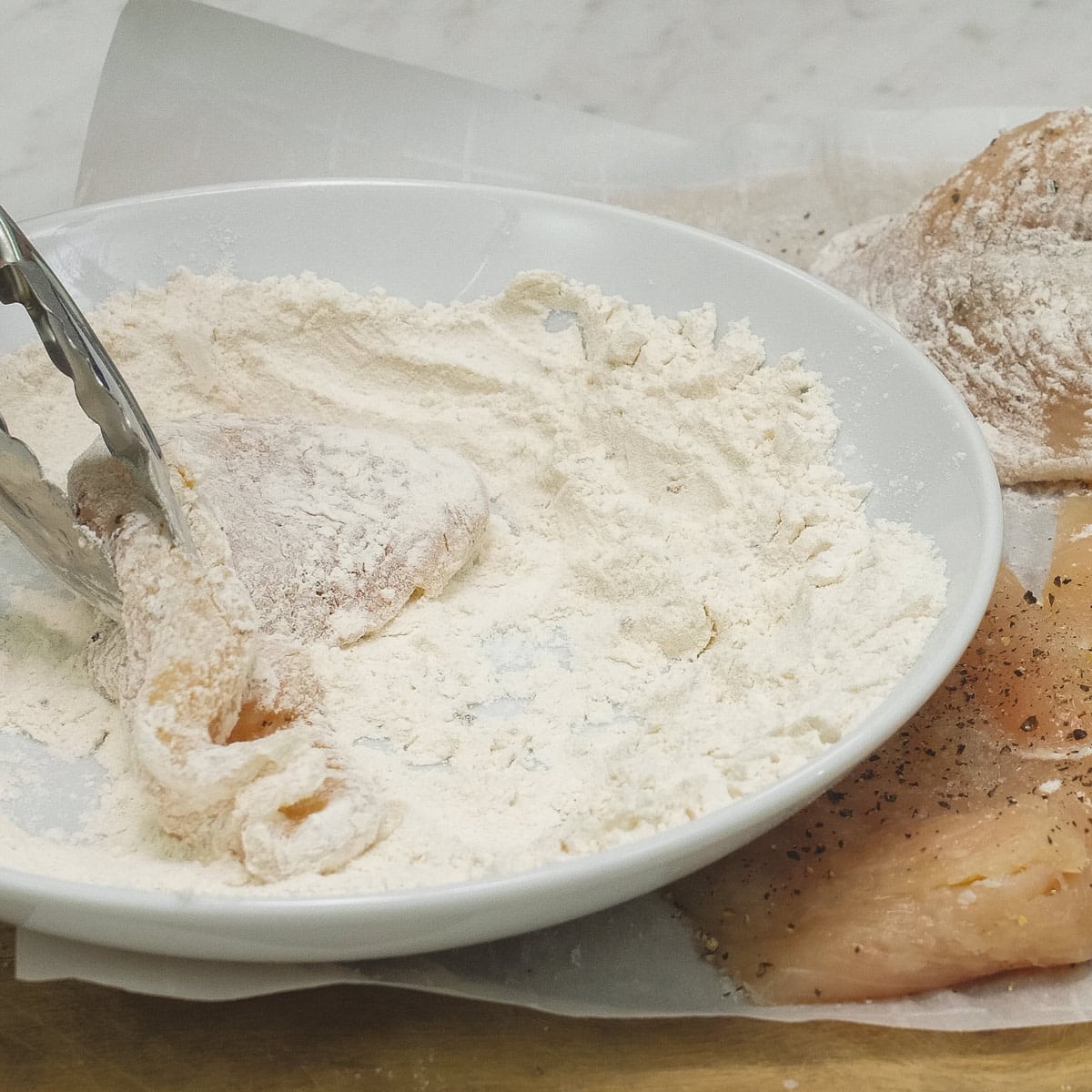 Dredging the chicken slices in the bowl of flour with the rest of them on the parchment paper.