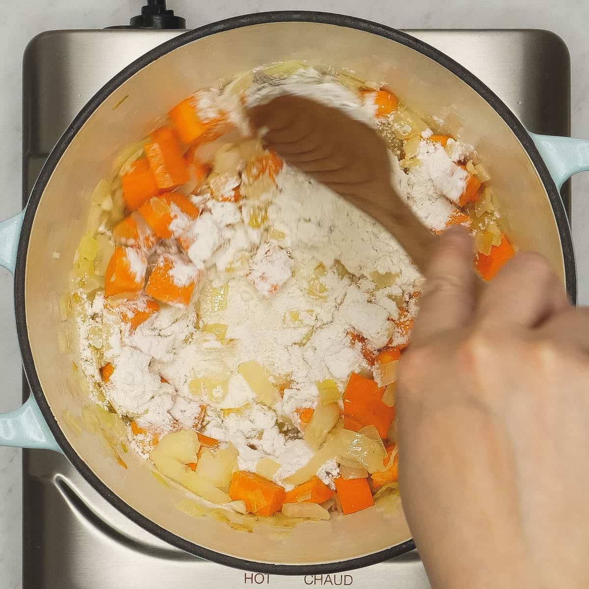 Mixing in the flour with the onions and carrots in the pot.