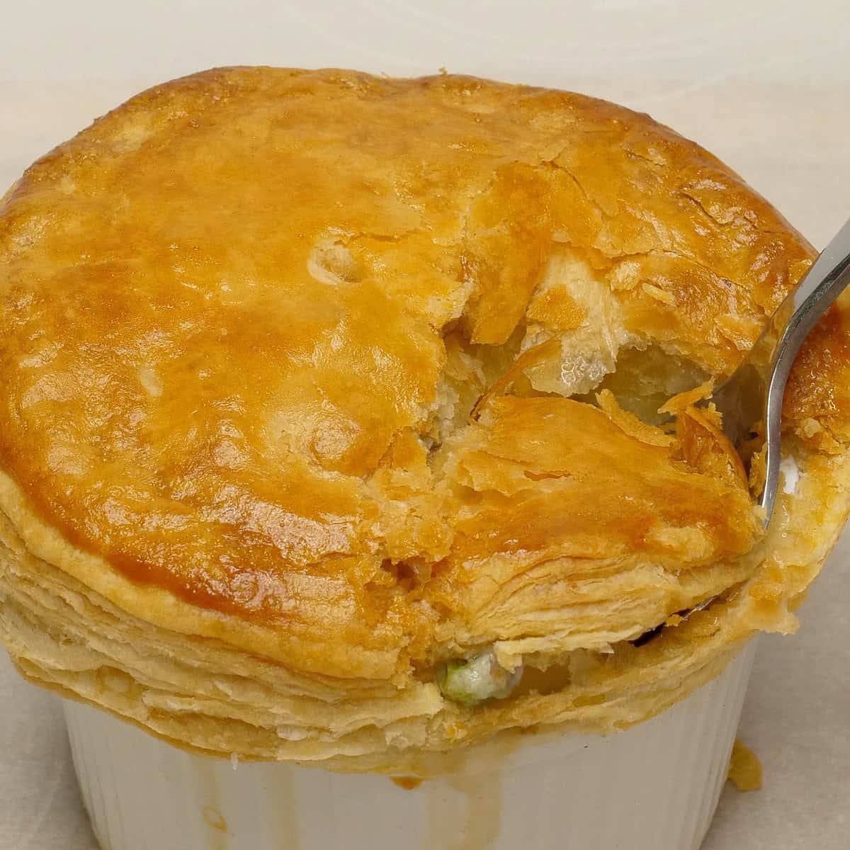 Scooping a portion of chicken pot pie with puff pastry from the ramekin using a spoon.
