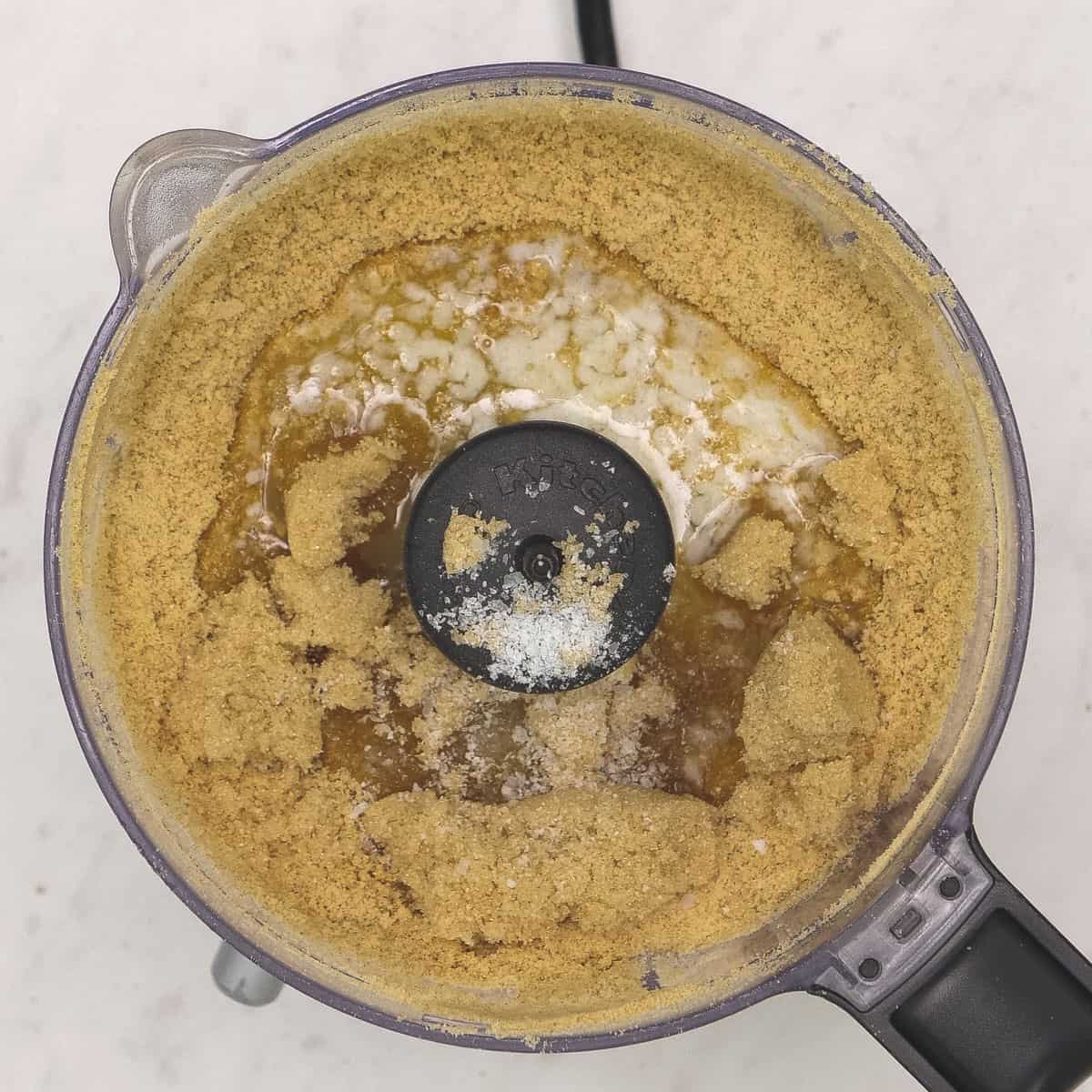 Crushed graham crackers with other ingredients in a food processor.