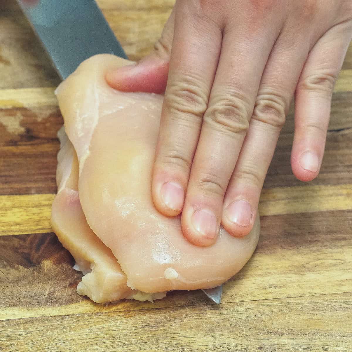Slicing chicken breast horizontally in half on a cutting board.