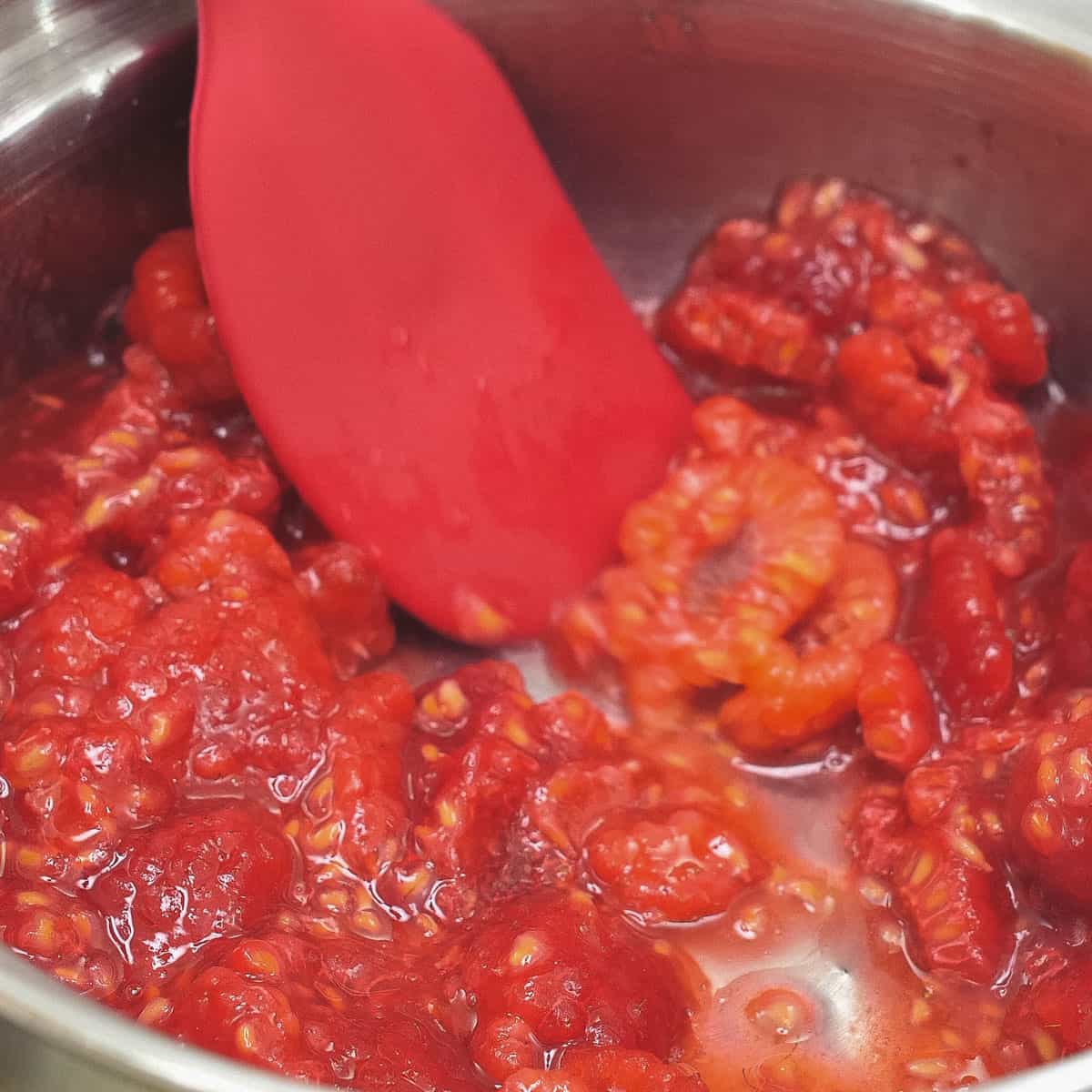 Mashing raspberries with a spatula in a small saucepan.