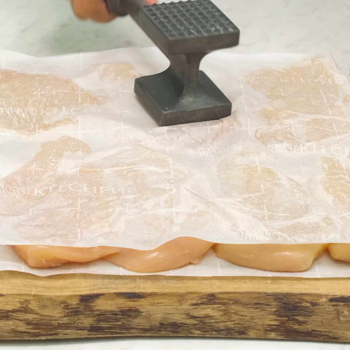Pounding the chicken in between the parchment paper with a meat mallet.