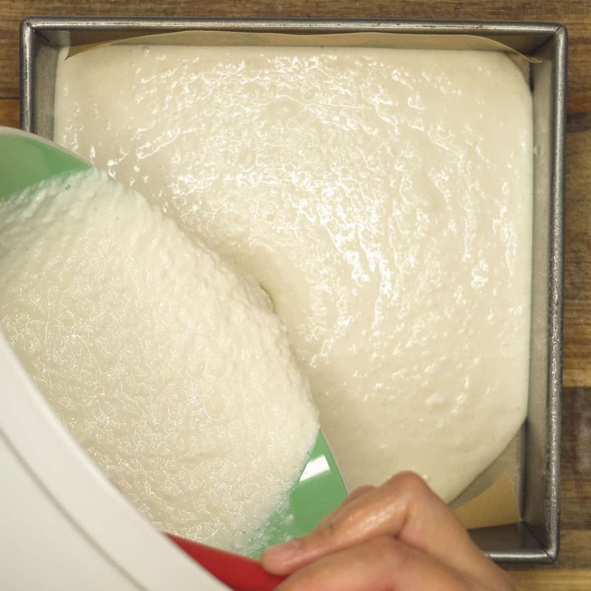 Pouring the cassava mixture into the parchment paper-lined pan. 