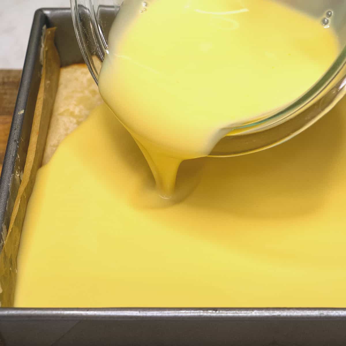 Pouring the custard mixture on top of the partially baked cassava cake. 