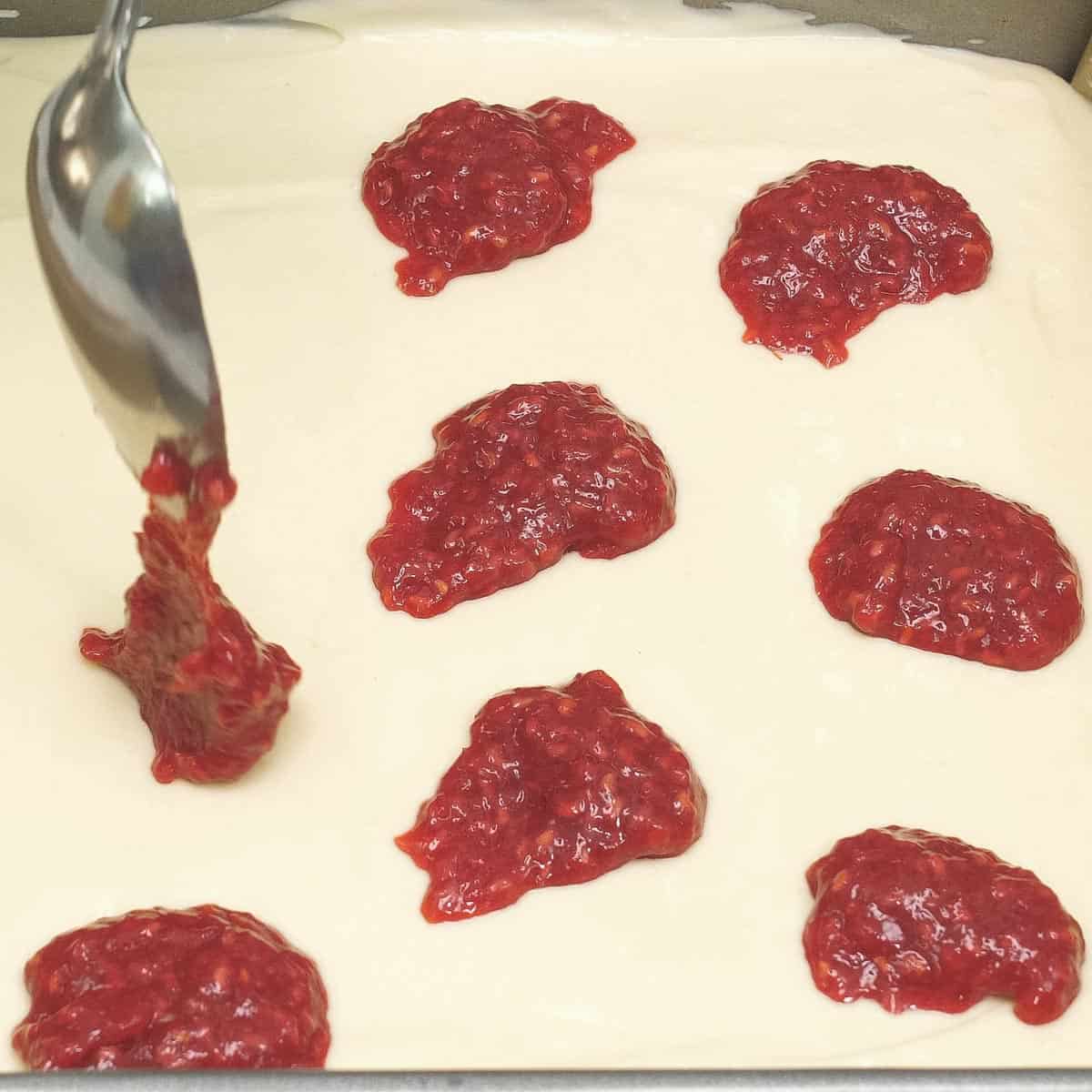 Adding dollops of raspberry sauce on the cheesecake batter.