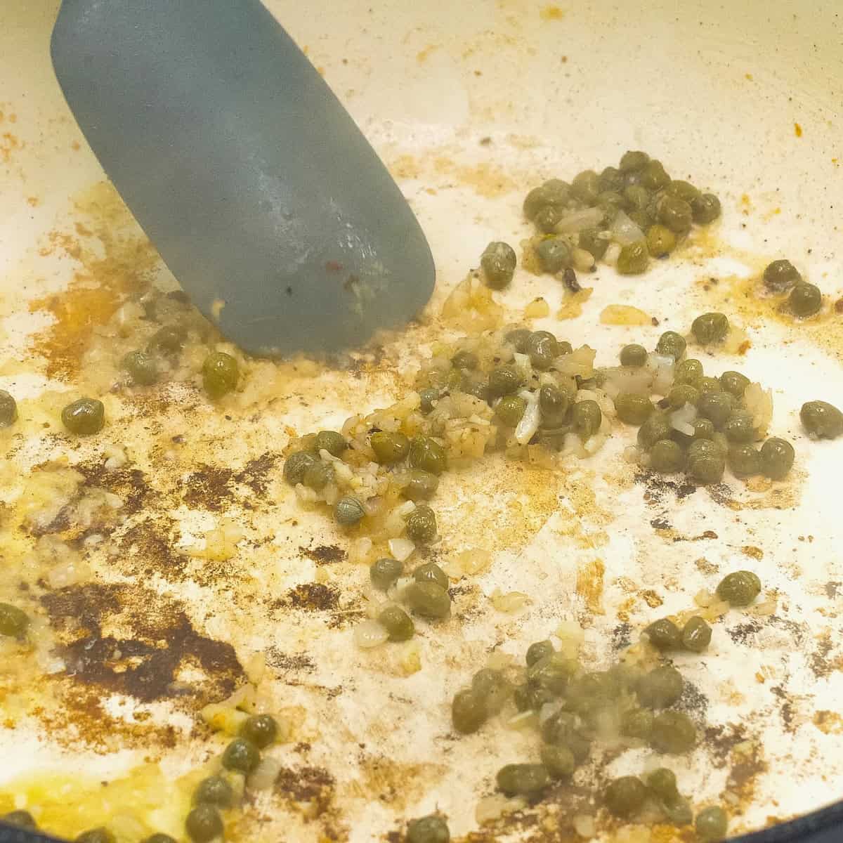 Sauteing shallots, garlic, and capers in the pan.