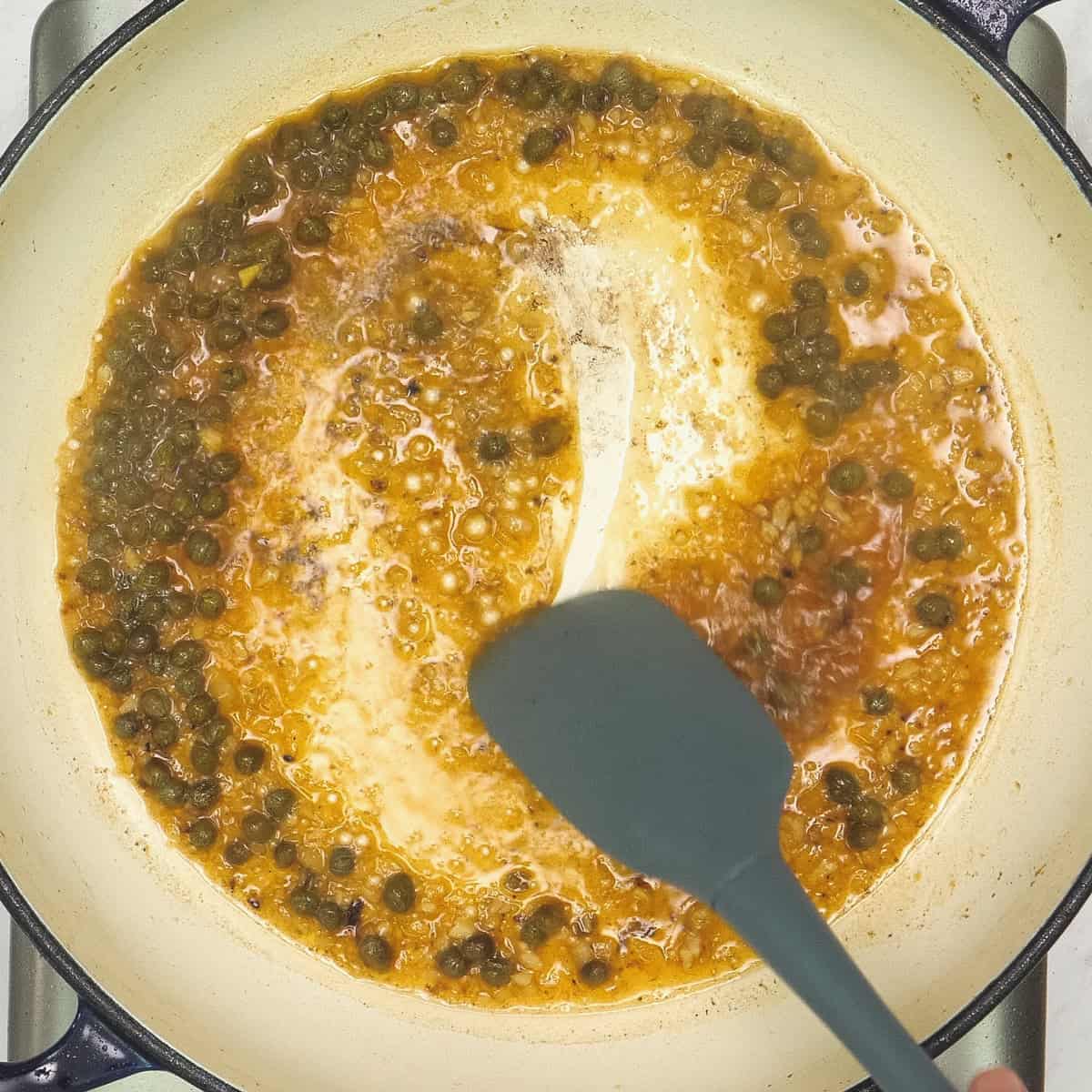 Scraping the browned bits off the pan using a spatula.
