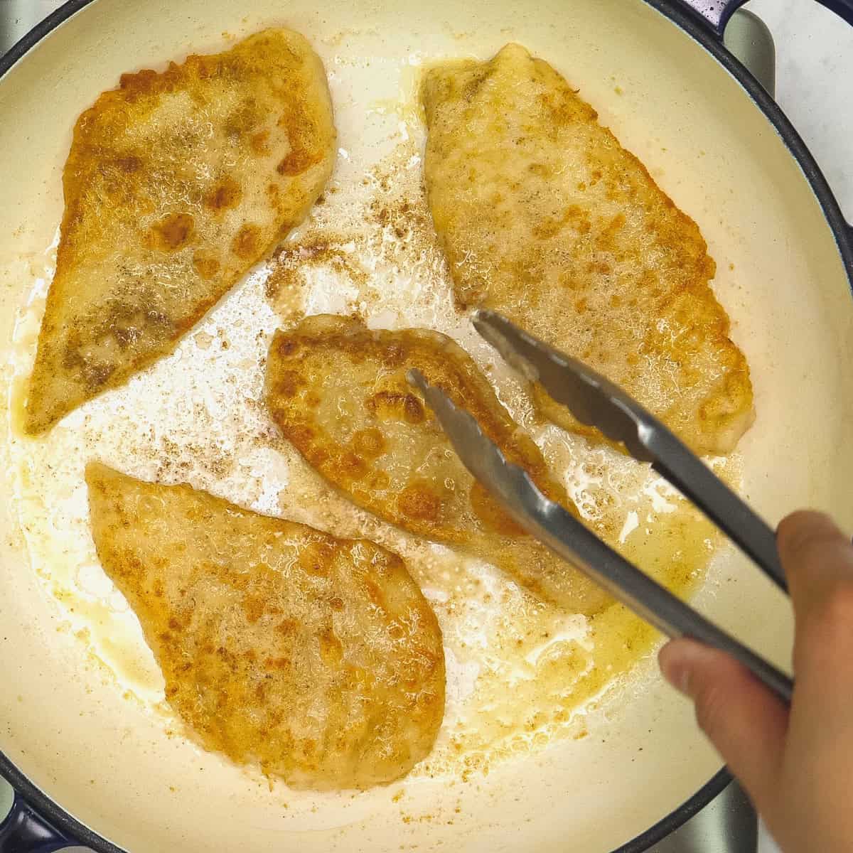 Turning the seared chicken in the pan using a pair of tongs.