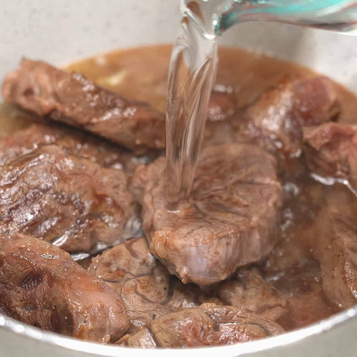 Pouring water over the meat in the pot.