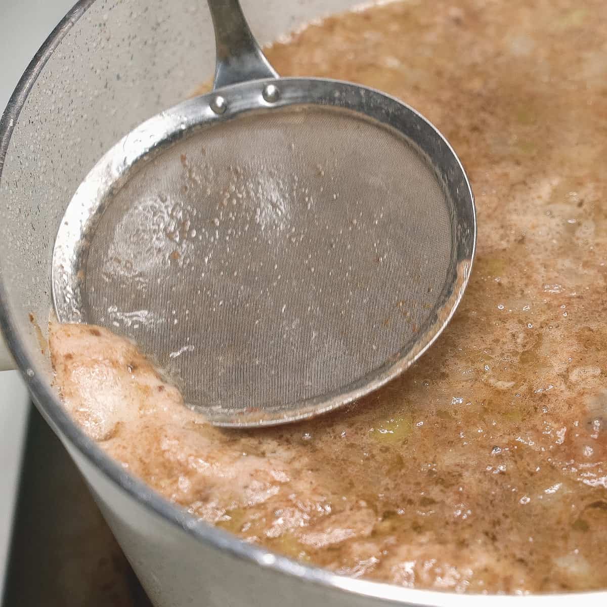 Skimming scum and fat off the surface using a skimmer.