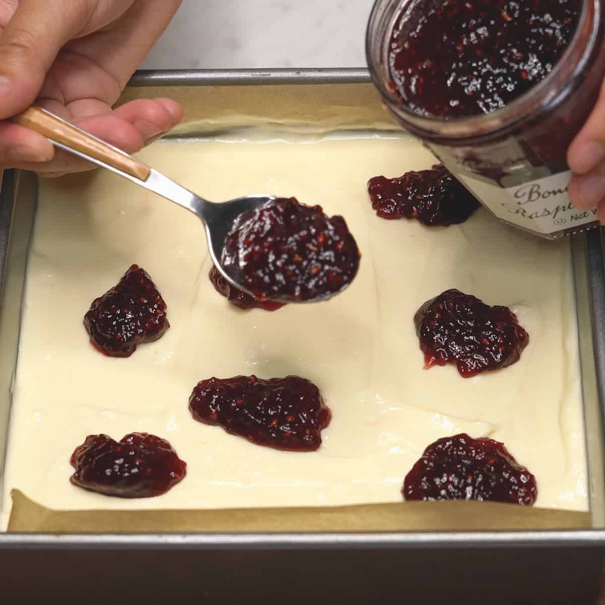 Adding dollops of store-bought jam on the cheesecake batter.