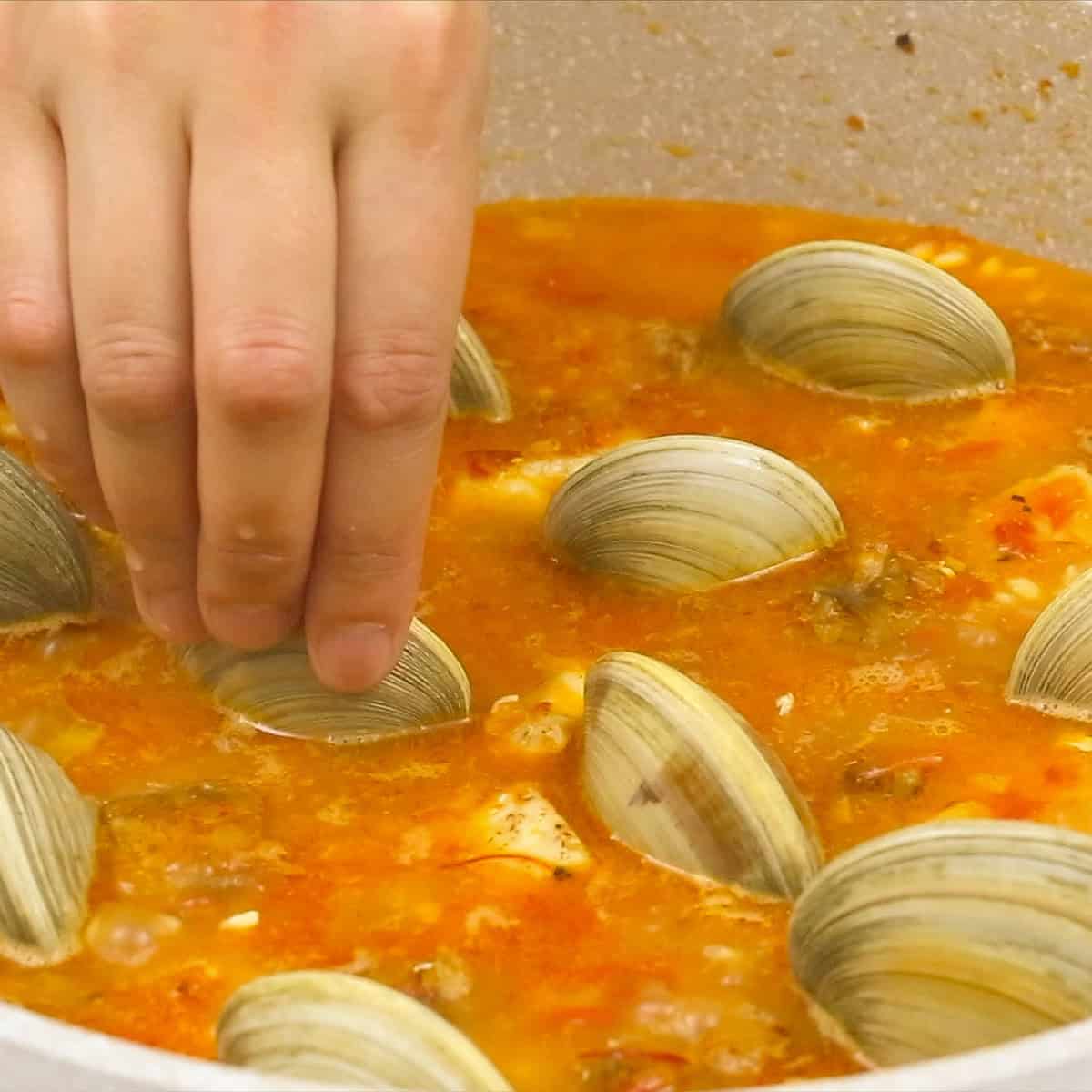 Adding clams to the Paella mixture in the pan.