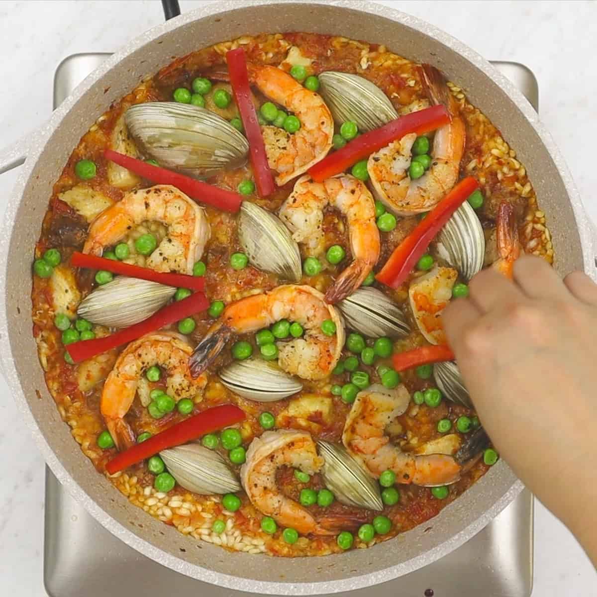 Adding vegetables to the paella in the pan.