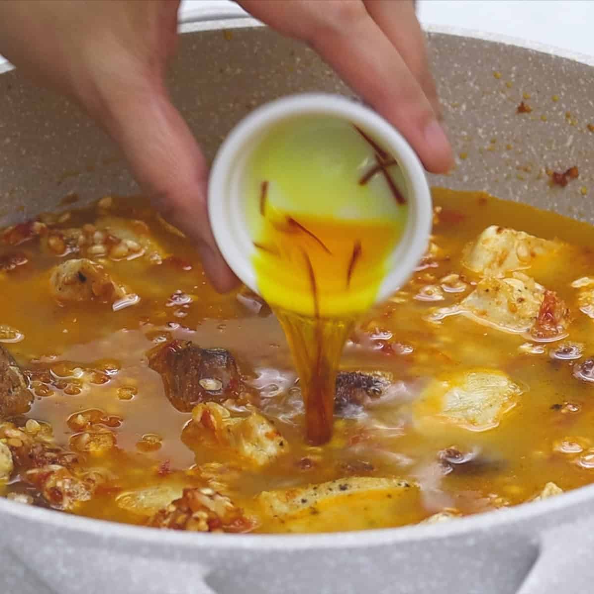 Adding saffron to the simmering Paella in the pan.