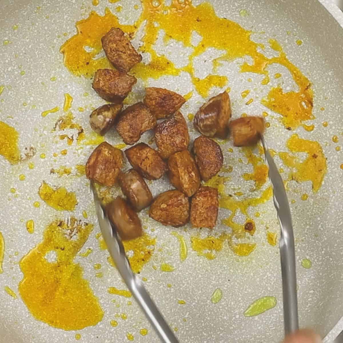 Searing pieces of chorizo in a pan.