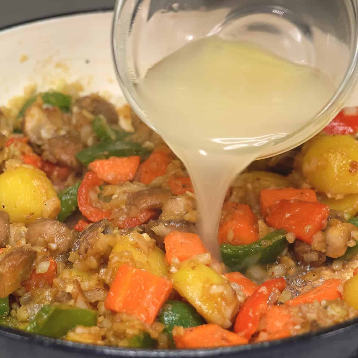 Adding chicken stock to the aromatics and vegetables in the saute pan.