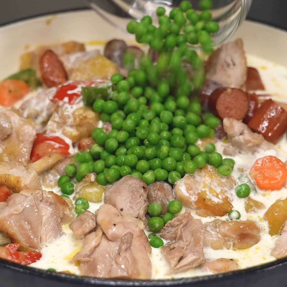 Adding peas to the meat and vegetables in the saute pan.