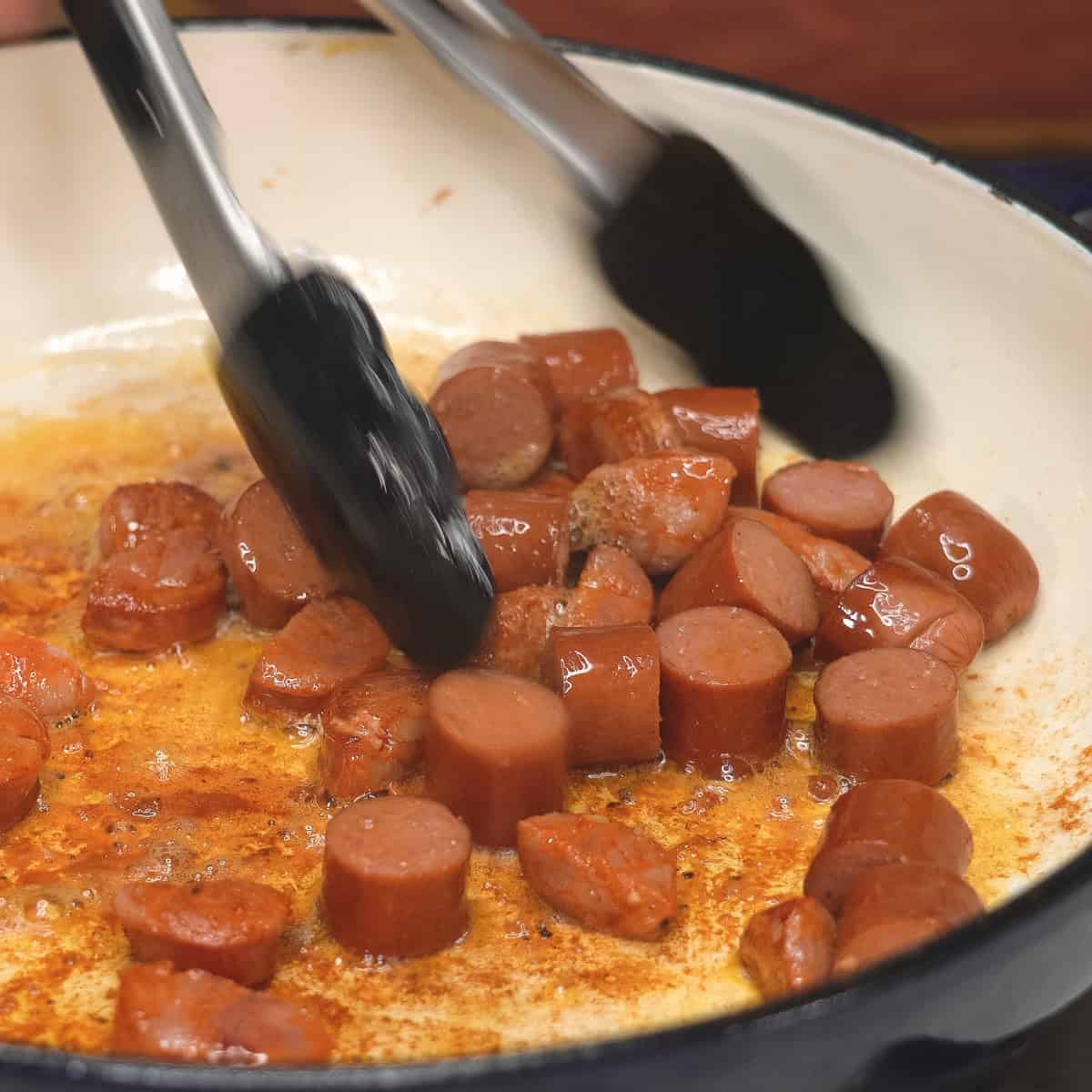 Searing chorizo and hotdogs in a saute pan.