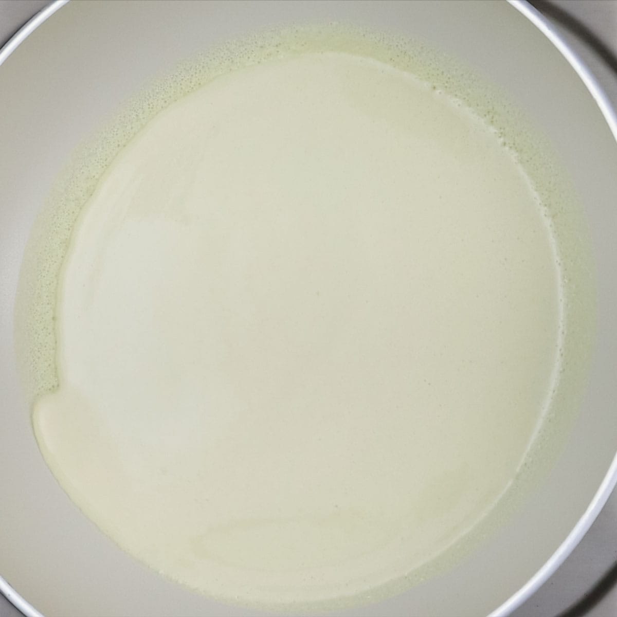 Spreading the crepe batter thinly on the pan.
