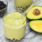 Avocado shake with boba in a glass with a straw.