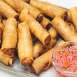 Lumpiang shanghai fried spring rolls with a vinegar dipping sauce on a plate.