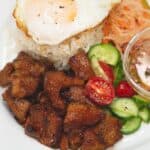 Pork Tocino Sweet Cured Pork with garlic rice topped with fried egg, vinegar dipping sauce, and salad on a plate.